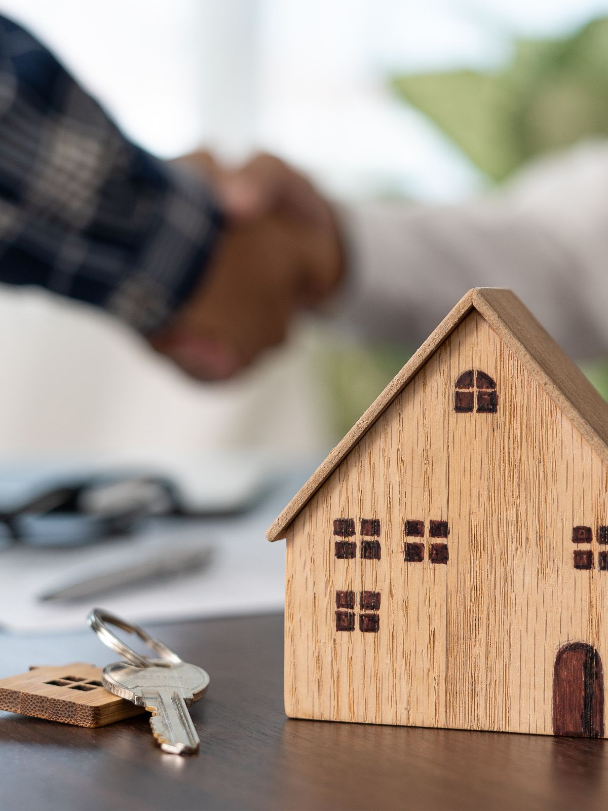 key and small home on a desk with people shaking hands in the background